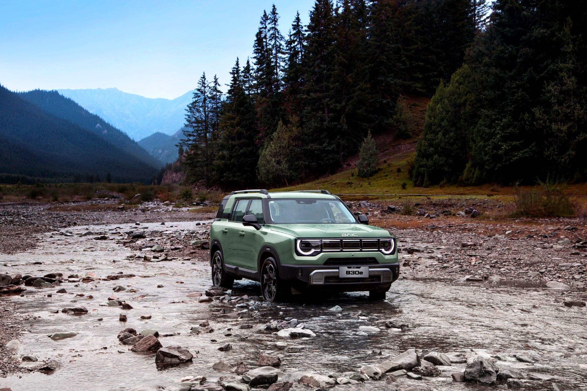 BAIC B30e driving through a rocky river bed in a forested valley